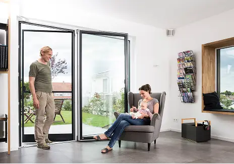 Fliegengitter-Pendeltür nach Maß für Balkon und Terrasse Familie im Wohnzimmer neben einer geöffneten Terrassentür mit maßgefertigter Fliegengitter-Pendeltür