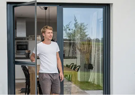 Fliegengitter-Drehtür nach Maß für Terrasse und Balkon Mann öffnet eine maßgefertigte Fliegengitter-Pendeltür an einer Terrassentür